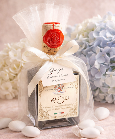 A personalized bottle of 1850
Dressing with Balsamic Vinegar of Modena gift set, wrapped in sheer white tulle with a cream ribbon and a red wax seal. The bottle features a custom Italian label with the names 'Martina & Luca' and the date '25 Aprile 2024'.