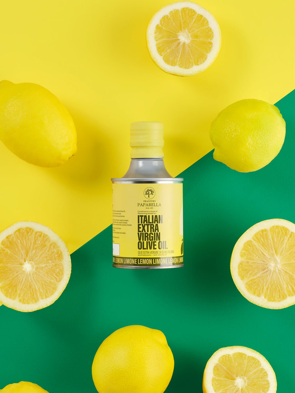 A bottle of Papiarella Italian Extra Virgin Olive Oil centered on a bright yellow and green background, surrounded by whole and sliced lemons.