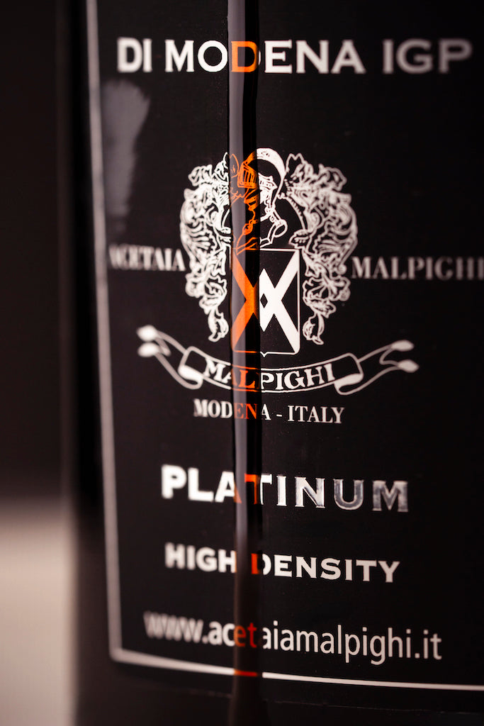 Close-up of a black bottle label for Di Modena IGP wine, featuring the Malpighi crest and the word 'PLATINUM' in white and orange text.