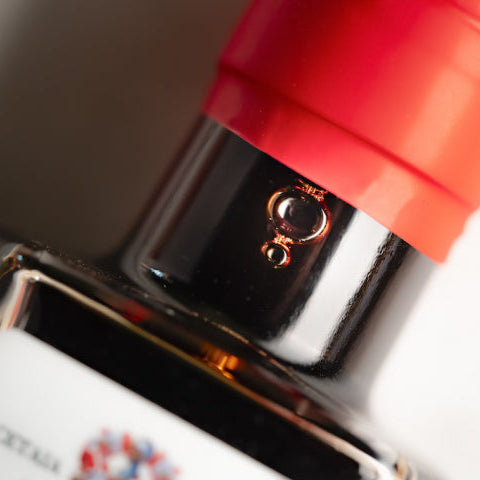 Close-up of a dark glass bottle with a bright red cap and a reflective black neck, showing a small metallic emblem on the collar.