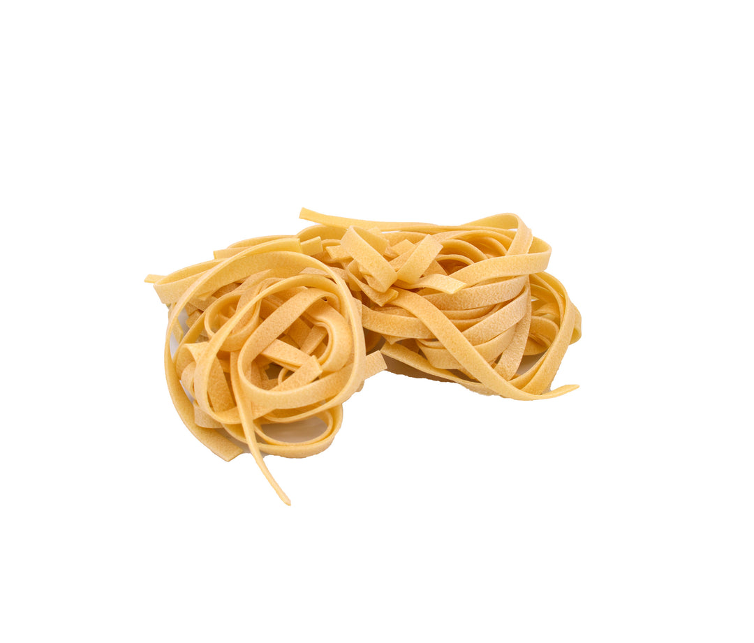 A small pile of uncooked flat pasta strands tagliatelle, in a light golden-yellow color, isolated on a solid white background.