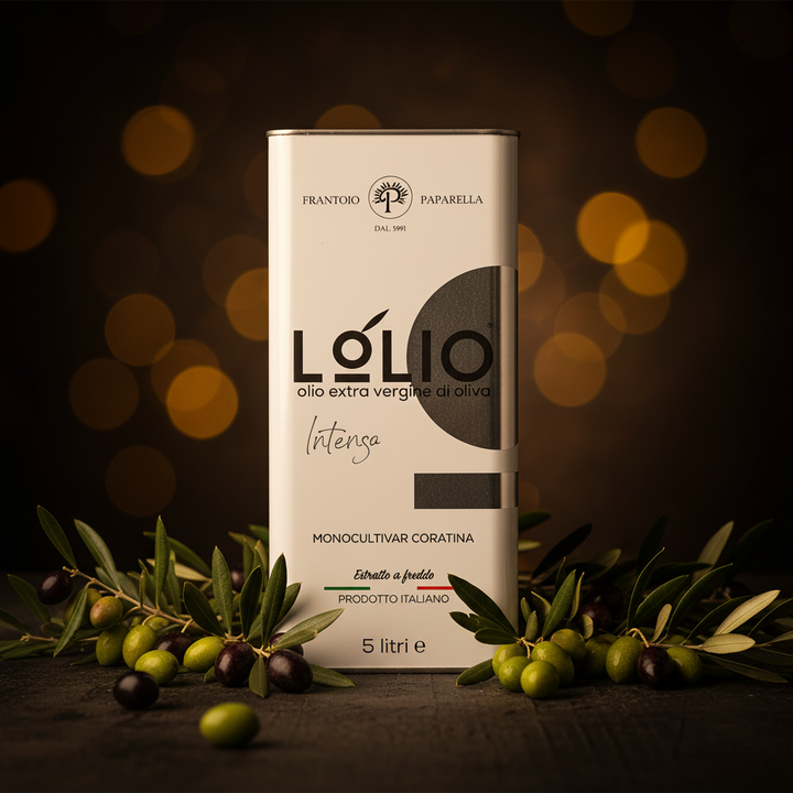 A 5-liter metal tin of Frantoro Paparella L'olio Intensa extra virgin olive oil stands on a dark tabletop, surrounded by green and black olives on branches, against a warm golden bokeh background.